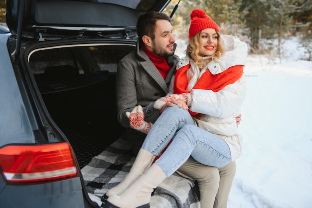 Happy couple sitting in open car back, having stop off. Romantic traveling concept. Winter forest.