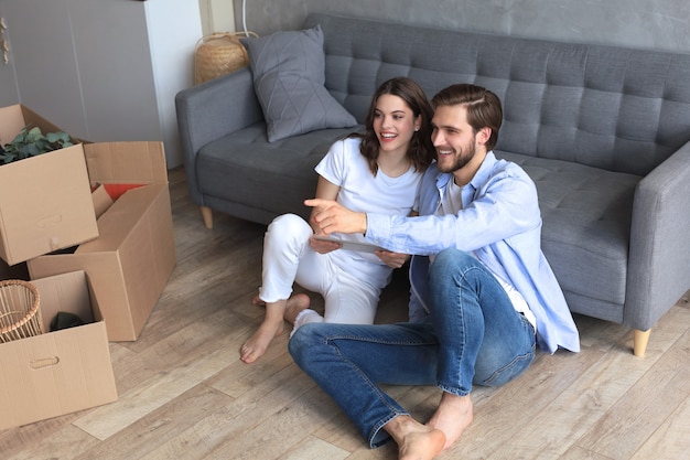 Happy couple sitting and planning new home decoration at home with a tablet at moving day, renovation and interior design for new house.