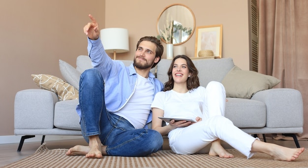 Happy couple sitting and planning new home decoration at home with a tablet, renovation and interior design for new house.