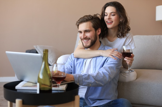 행복한 커플은 거실 바닥에 앉아 휴식을 취하고 온라인 쇼핑을 위해 노트북을 함께 사용하고 영화를 봅니다.