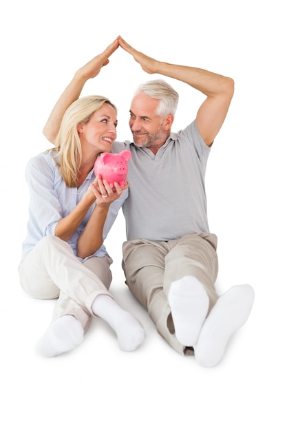 Happy couple sitting and sheltering piggy bank