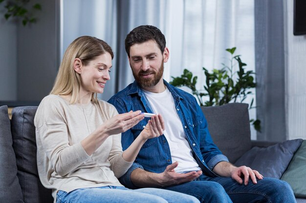 Photo happy couple sitting on sofa at home man and woman got positive pregnancy test