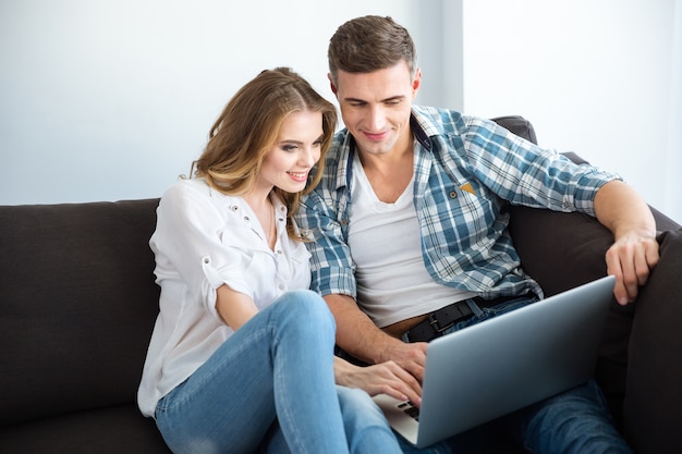 Happy couple sitting on sofa and using laptop together