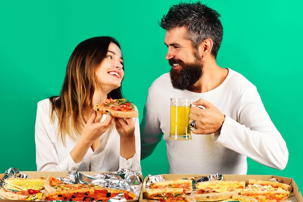 Happy couple sitting at table eating pizza and drinking beer\
having fun together food delivery