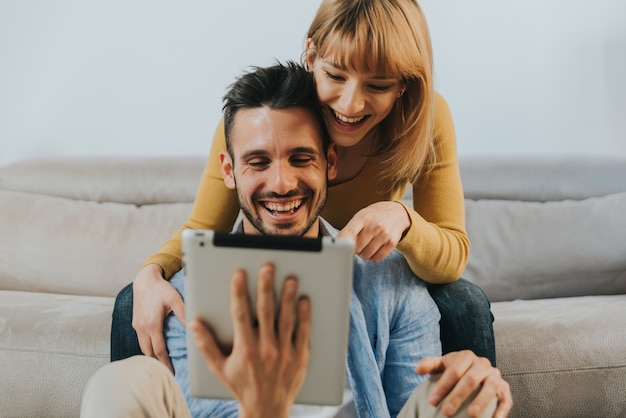 Happy couple smiling using digital tablet at home.