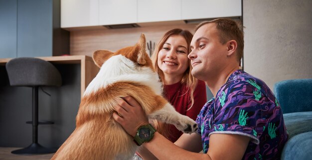 Photo happy couple spending time with cute corgi at home