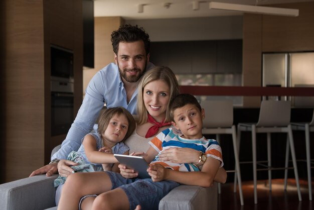 happy couple spending time with kids using tablet computer on an armchair at home