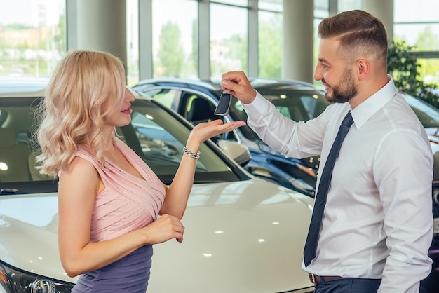 Happy couple stand in front of new car man covered wife eyes in showroomsurprised gift automobile