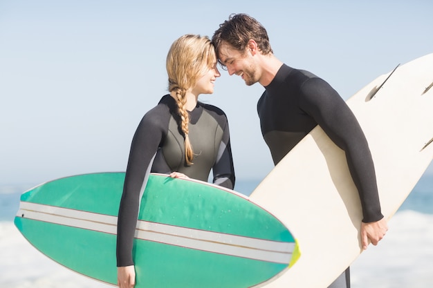 Happy couple standing head to head with surfboard