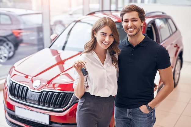 Photo happy couple standing near new car in dealership