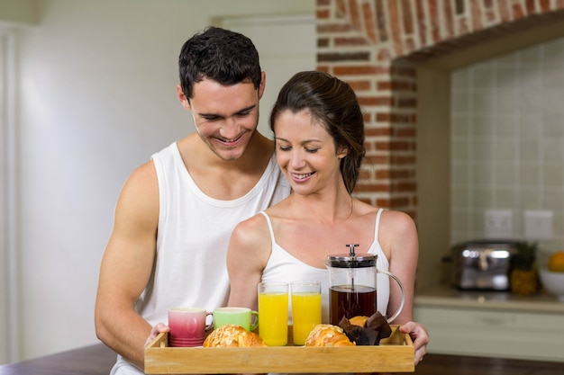 Coppie felici che stanno insieme nella cucina con il vassoio della prima colazione sul vassoio