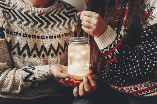 크리스마스 트리 해피 홀리데이 대기 축제 순간 메리 크리스마스와 새해 복 많이 받으세요 개념에 축제 방에서 등불을 들고 세련된 스웨터에 행복한 커플