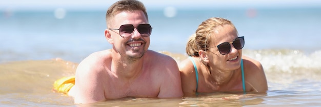 Happy couple in sunglasses lies on beach in sea