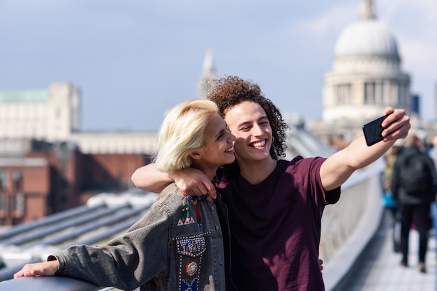 Photo happy couple taking a selfie photograph on london's millennium bridge