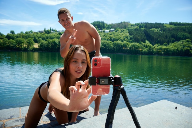 A happy couple taking a selfie on the shore with a forest in the background