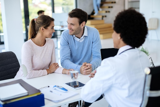 Happy couple talking while having appointment with a doctor at the clinic