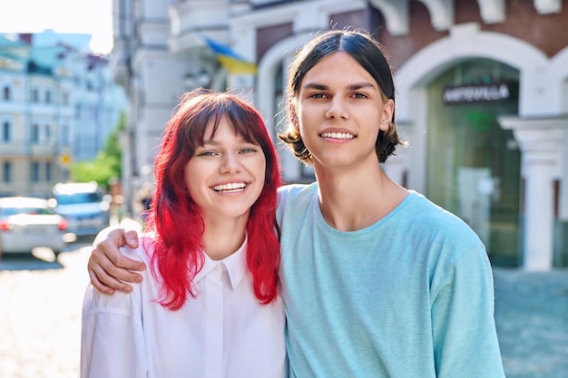 Happy couple of teenage friends hugging looking at camera on city street