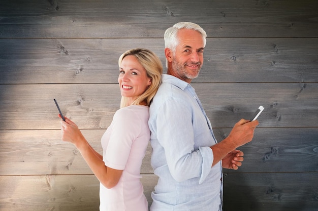 Happy couple texting on their smartphones against bleached wooden planks background