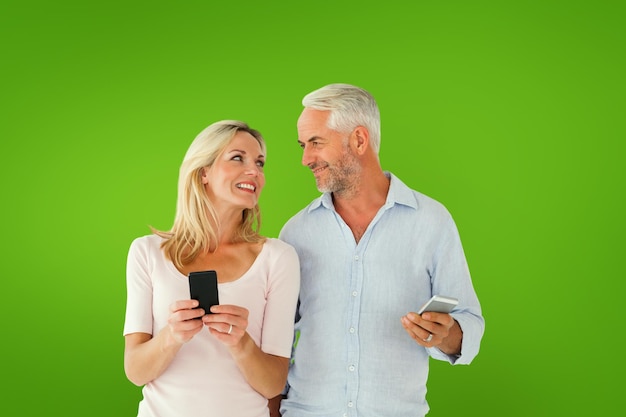 Happy couple texting on their smartphones against green vignette