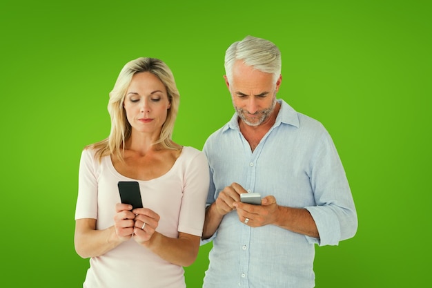 Happy couple texting on their smartphones against green vignette