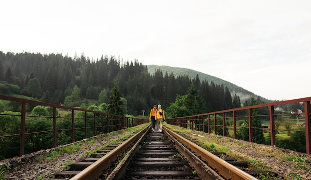 Happy couple of tourists holding hands walking on the railway track on the bridge