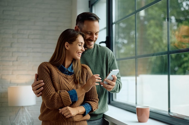 Happy couple using app on mobile phone by the window