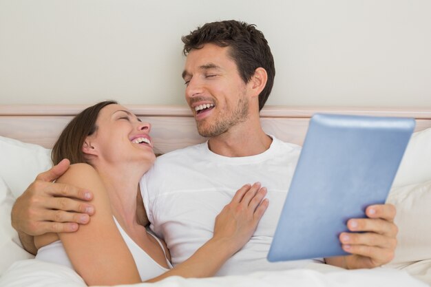 Photo happy couple using digital tablet in bed