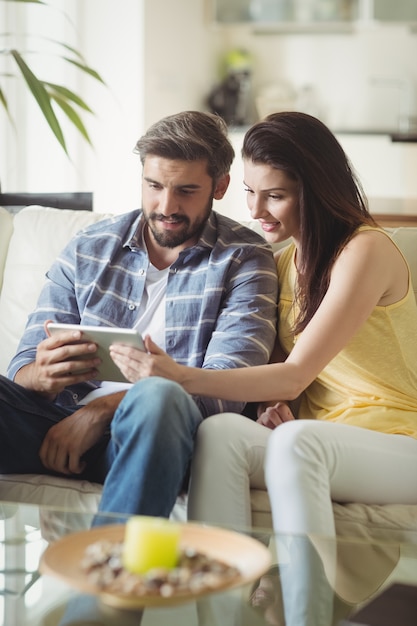 Happy couple using digital tablet while relaxing on sofa