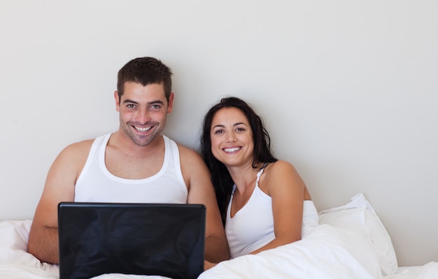 Счастливая пара, используя ноутбук, улыбаясь на камеру