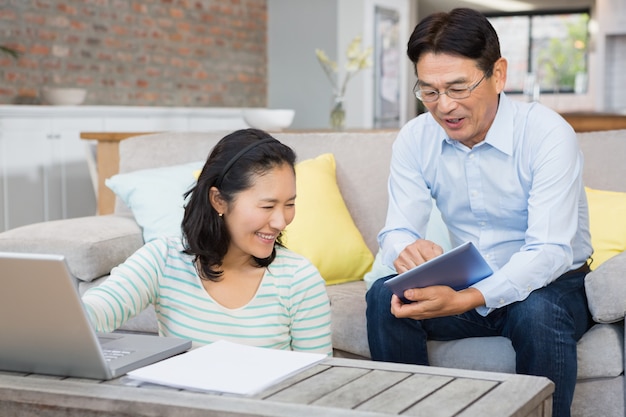 Happy couple using laptop and tablet in the living room