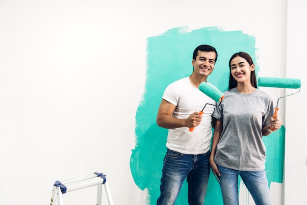 Happy couple using paint roller and painting wall