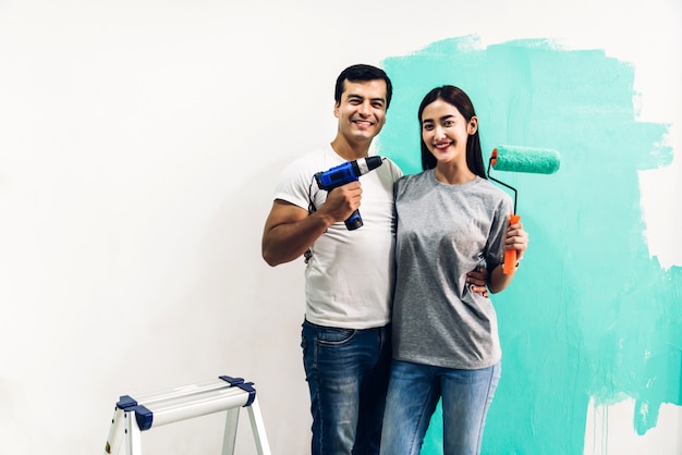 Happy couple using a paint roller and painting walls in their new home