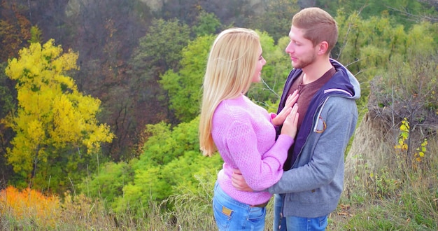 Happy couple on walk in autumn forest young girl kisses her boyfriend looks happy right into camera ...