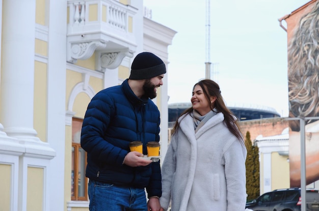 Happy couple walking in city. Young business man in a blue jacket, beard. cute woman in long coat.