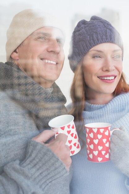 Happy couple in warm clothing holding mugs