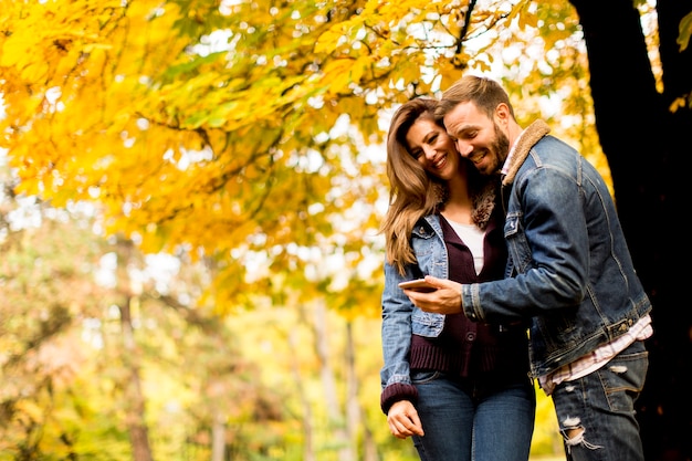 スマートフォンを見て、秋の公園に立っている幸せな夫婦