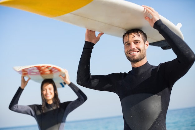 Foto coppia felice in mute umide con tavola da surf in una giornata di sole