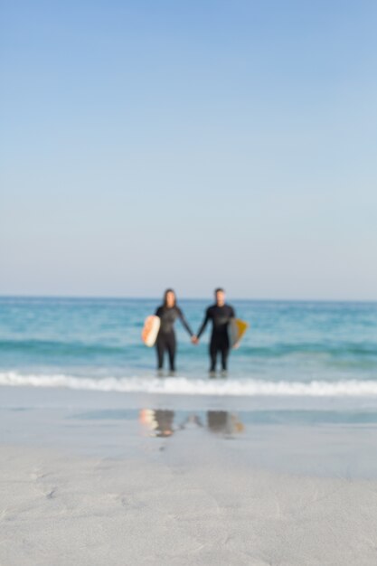 Happy couple in wetsuits with surfboard on a sunny day