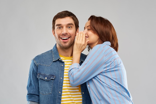 happy couple whispering over grey background