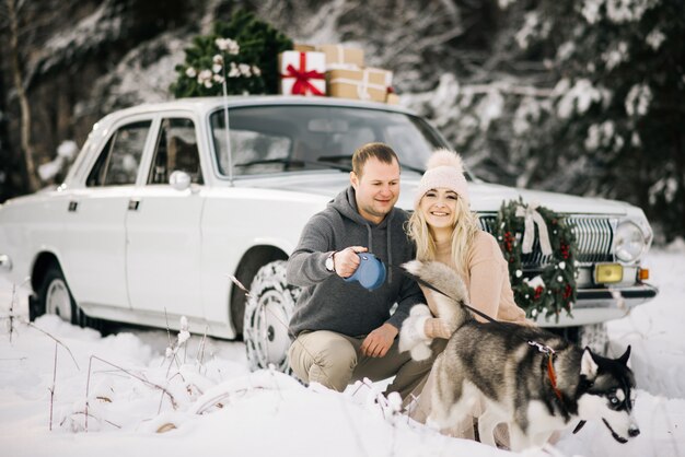 Happy couple on a winter day with retro car and husky