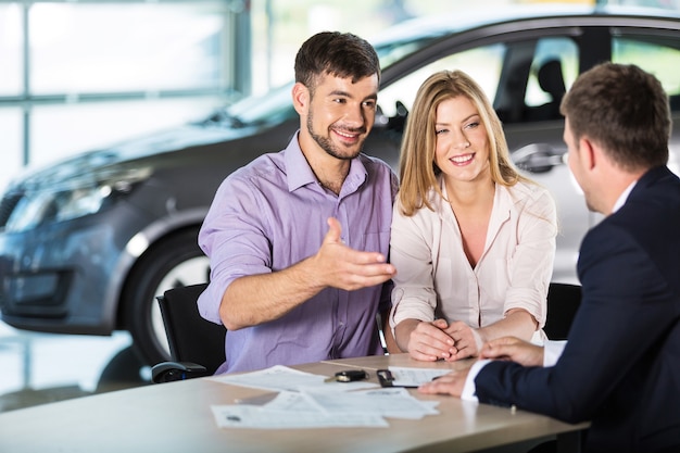 Photo happy couple with car dealer in auto show or salon