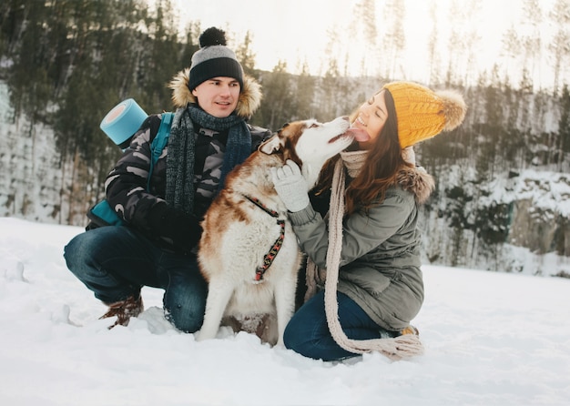 Le coppie felici con il cane haski al parco naturale della foresta nella stagione fredda