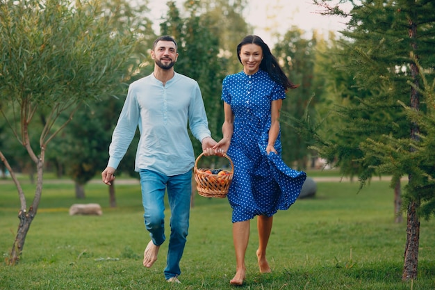 Счастливая пара с фруктами в корзине для пикника, бегущей в парке.