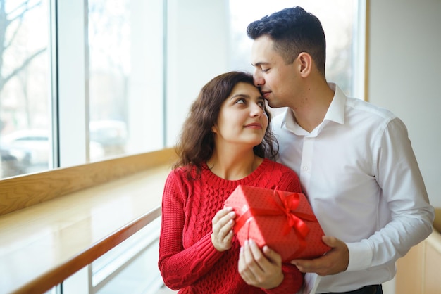 Счастливая пара с подарком обнимает Красная подарочная коробка в руках влюбленной пары День Святого Валентина
