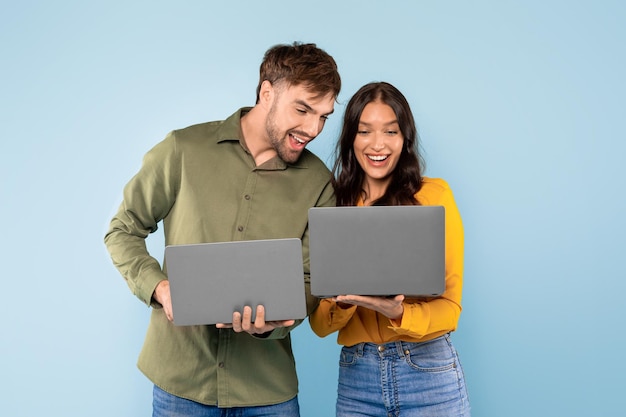 Happy couple with laptops sharing a screen on blue backdrop