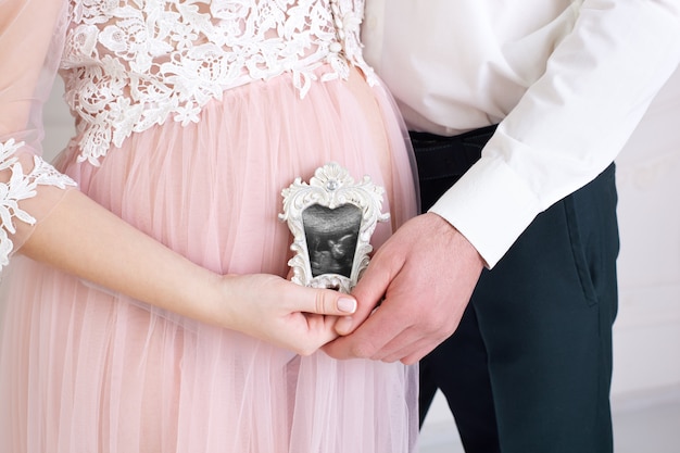 Happy couple with pregnancy news. Pregnant couple holding in the hands ultrasound scan of their baby. Healthy parents holding in hands on belly photo of their child.