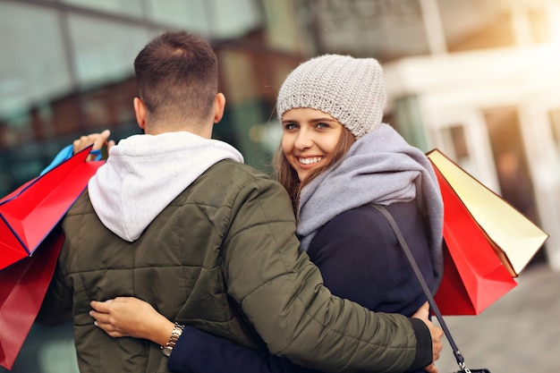 happy couple with shopping bags after shopping in city smiling and hugging