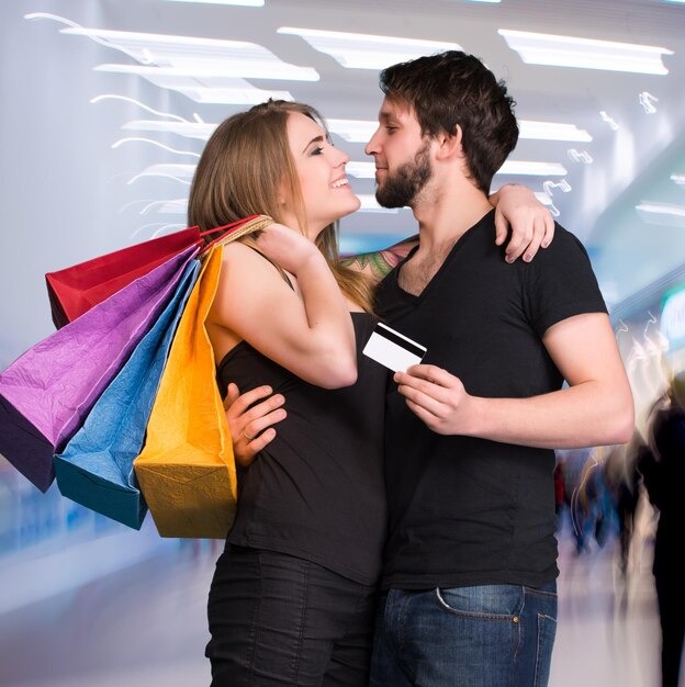 Happy couple with shopping bags at the mall. Man holding credit card