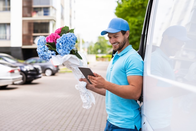 Happy courier with a tablet pc during flowers delivery