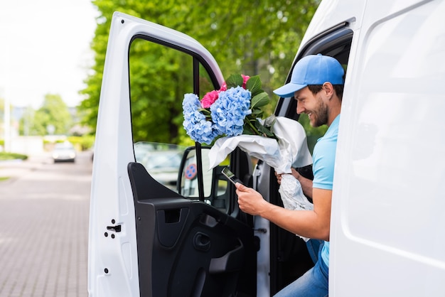 Happy courier with a tablet PC during flowers delivery